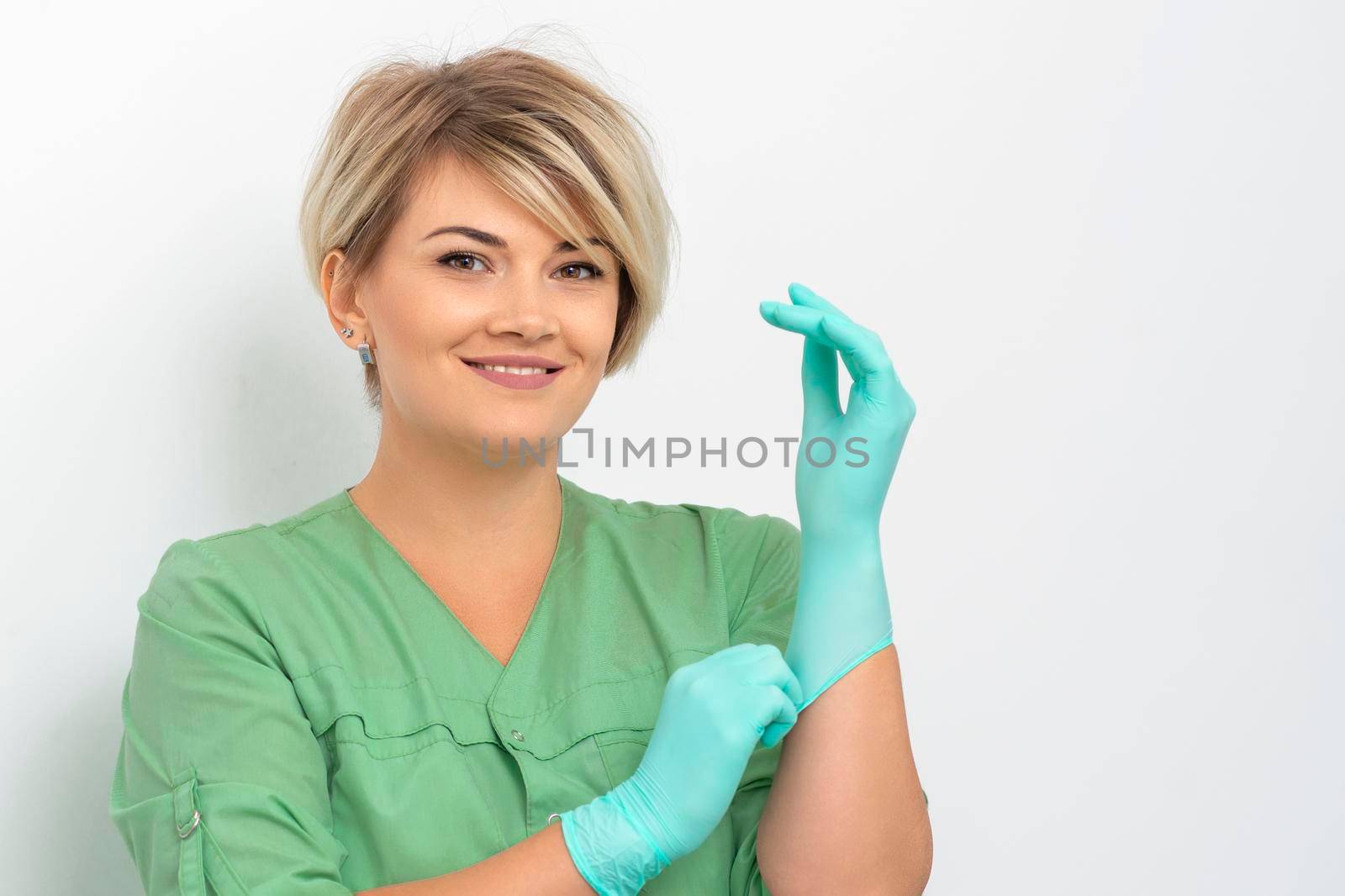 Doctor beautician puts on sterile blue gloves smiling prepares to receive clients on white