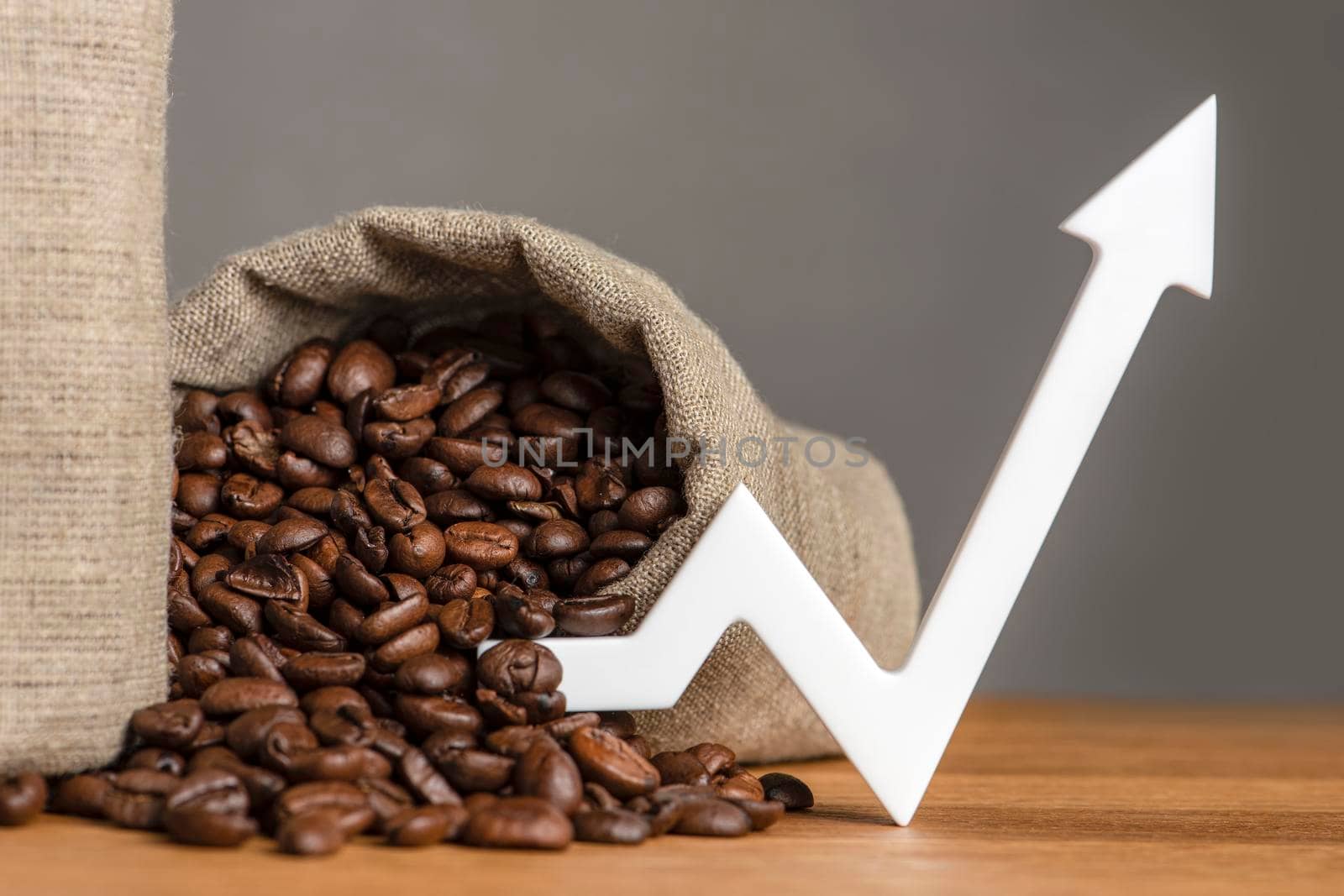 A bag of coffee beans and a chart arrow pointing up. The cost of coffee in the markets of the world. The concept of the growth of the cost of coffee beans.
