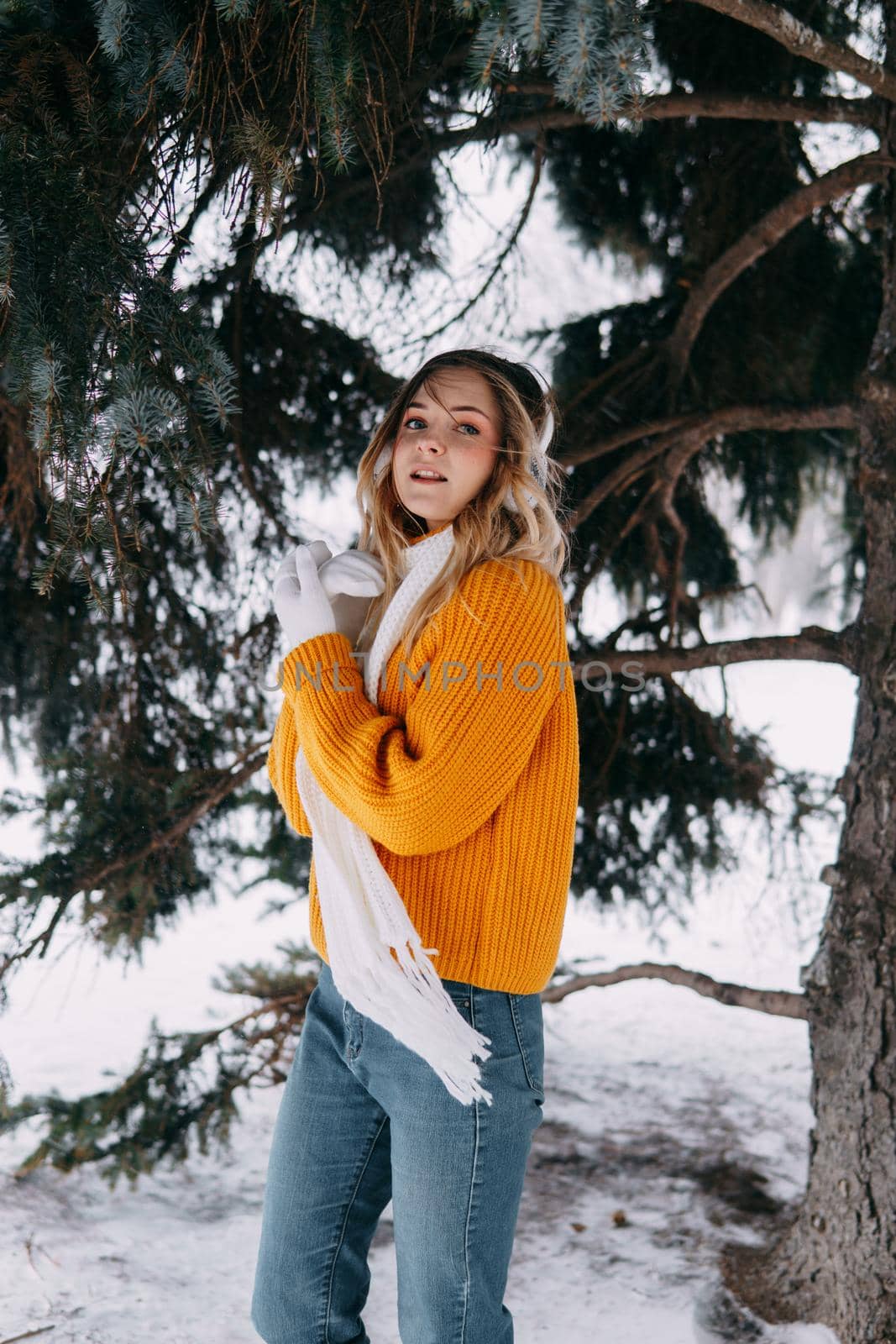 Teen blonde in a yellow sweater outside in winter. A teenage girl on a walk in winter clothes in a snowy forest.