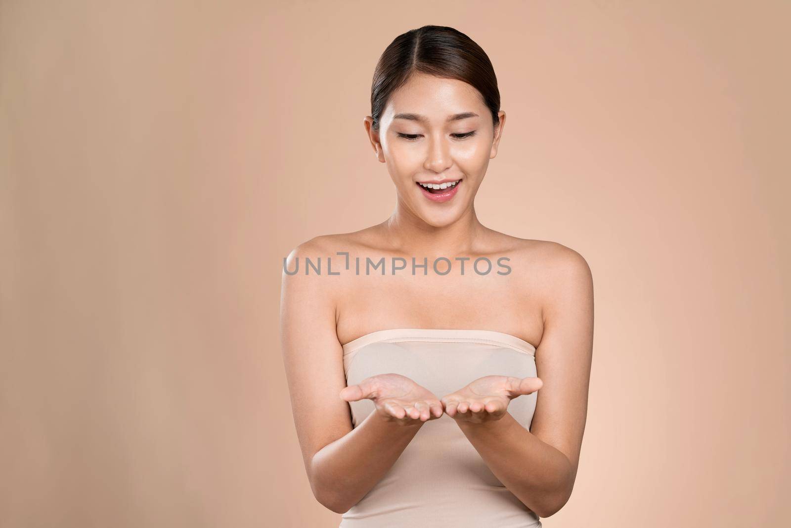 Portrait of ardent woman looking at camera, holding empty space for product, advertising text place, isolated background. Concept of healthcare advertising for skincare, beauty care product.
