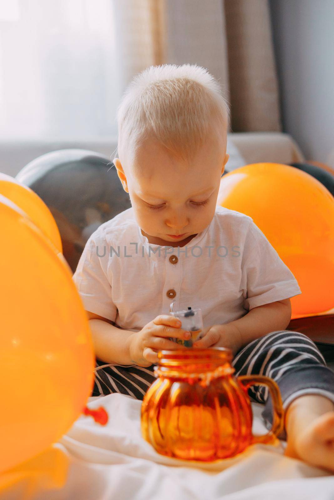 Children's Halloween - a boy in a carnival costume with orange and black balloons at home. Ready to celebrate Halloween