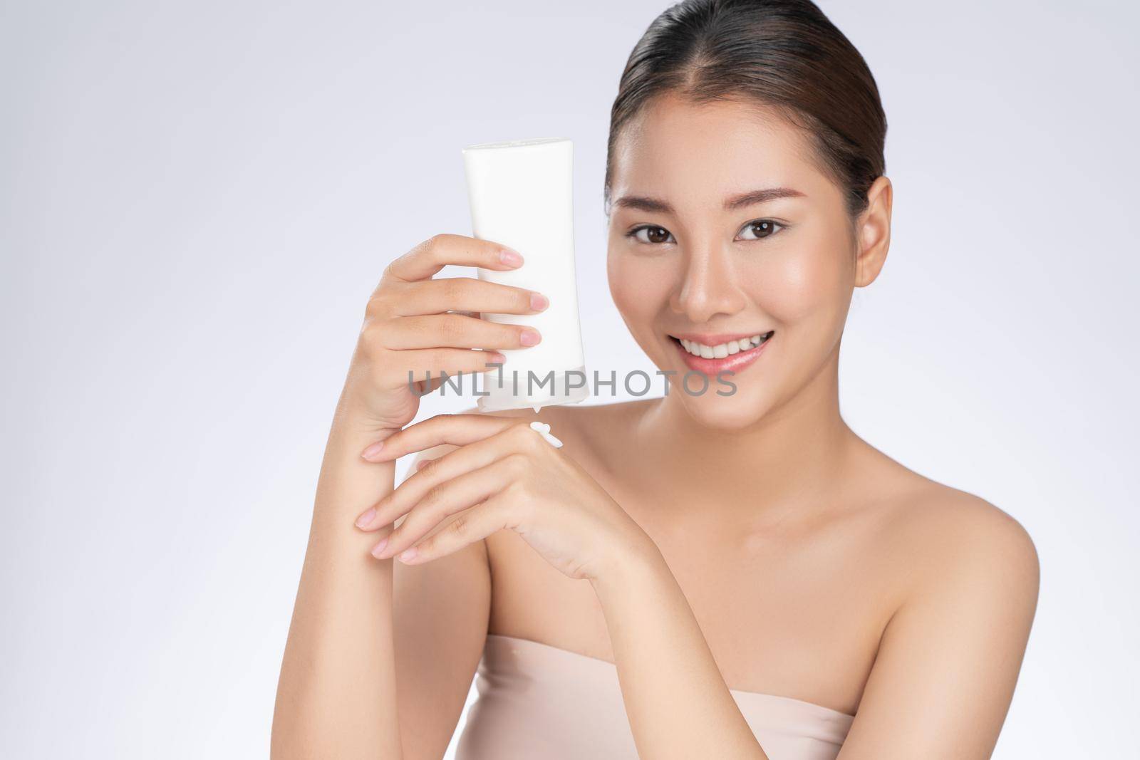 Gorgeous woman smiling holding mockup product for advertising text place, light grey background. Concept of healthcare for skin, beauty care product for advertising.