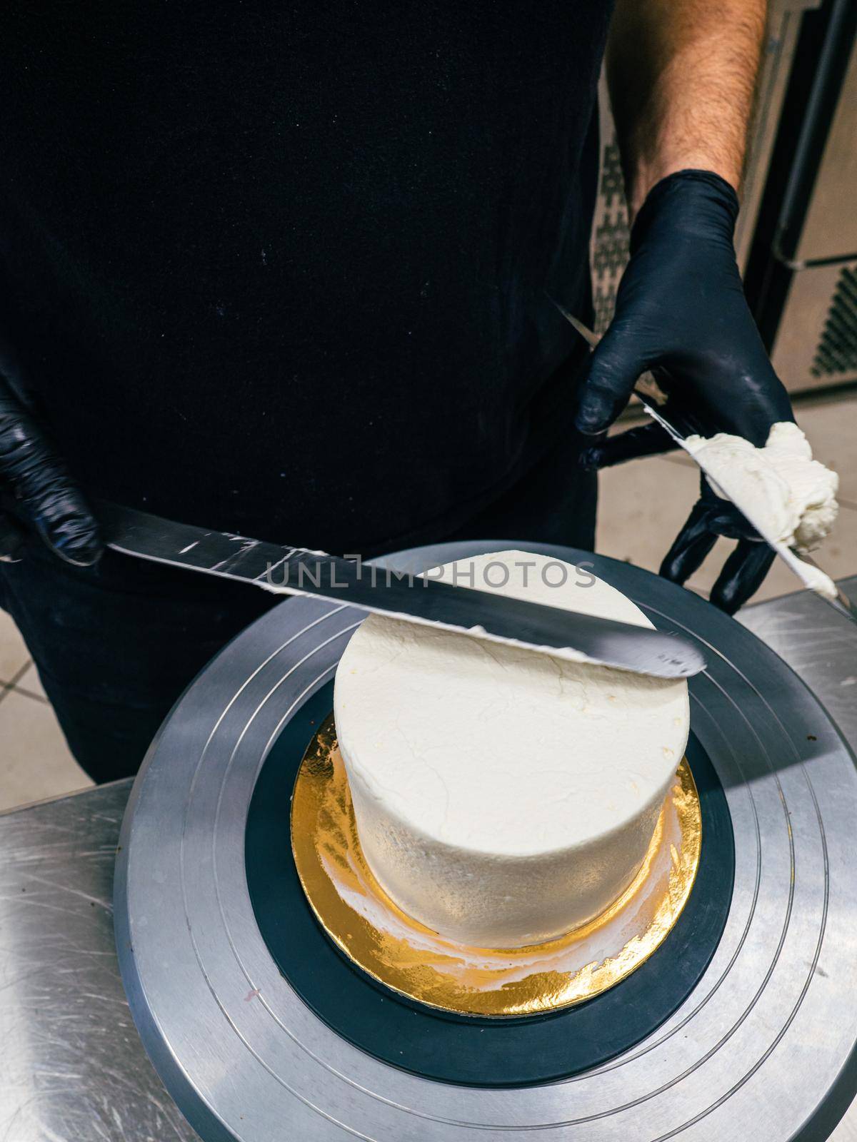 Decorator using spatula and scraper to smooth buttercream on a frosted cake