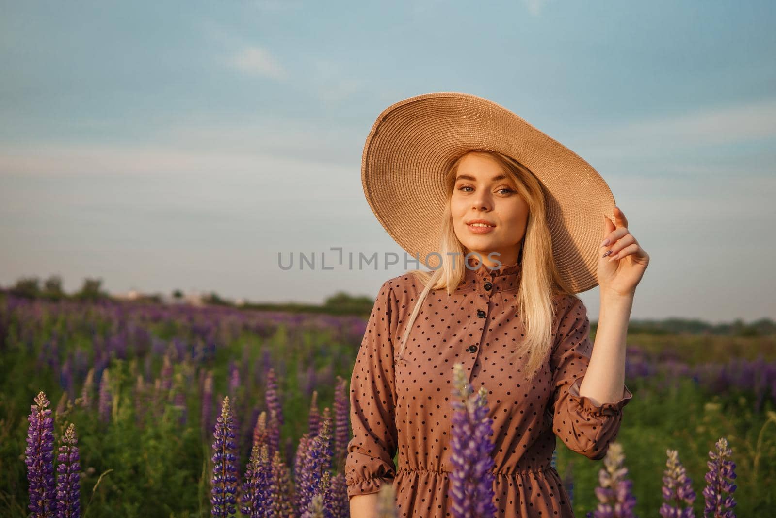 A beautiful woman in a straw hat walks in a field with purple flowers. A walk in nature in the lupin field.