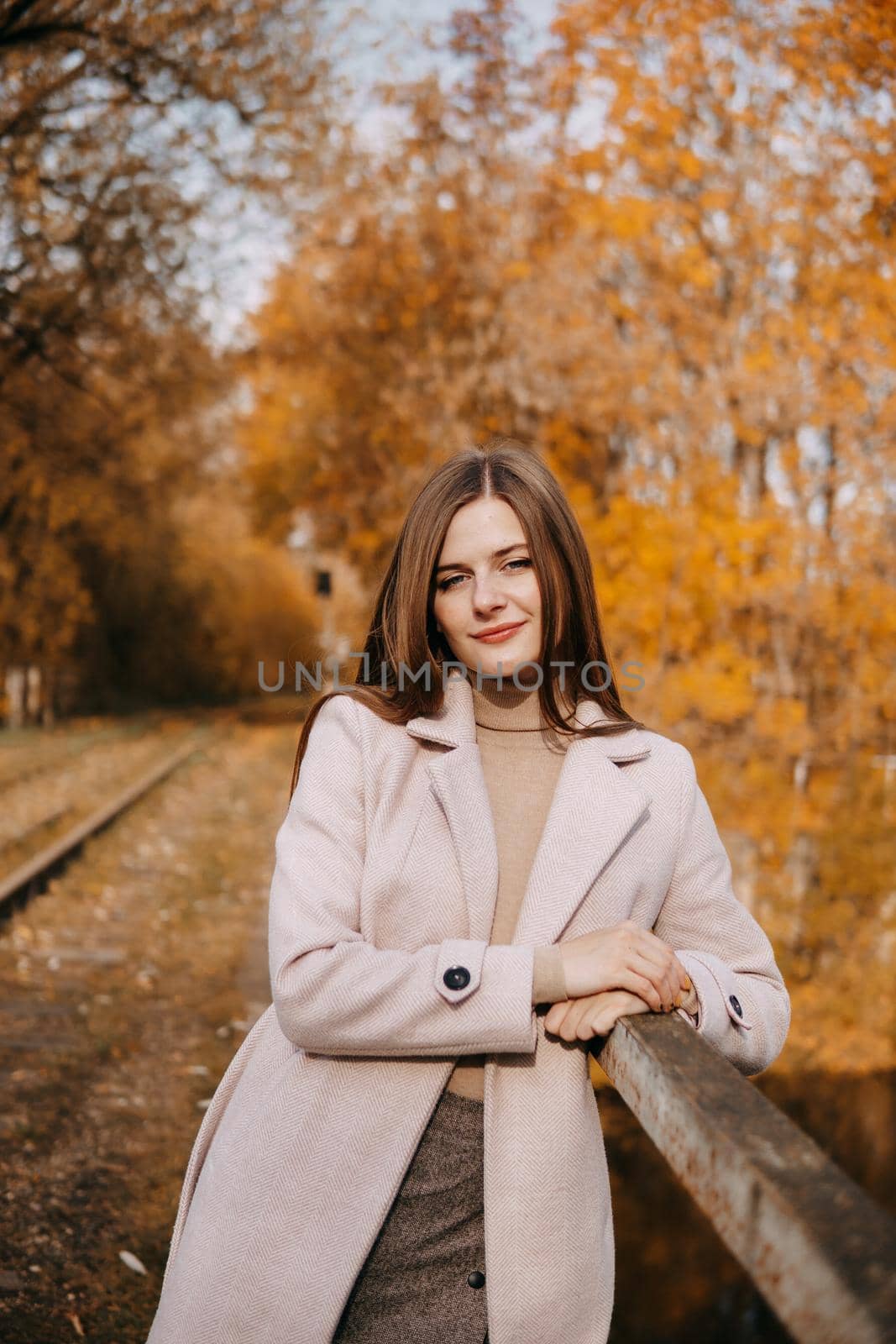 A beautiful long-haired woman walks through the autumn streets. Railway, autumn leaves, a woman in a light coat.