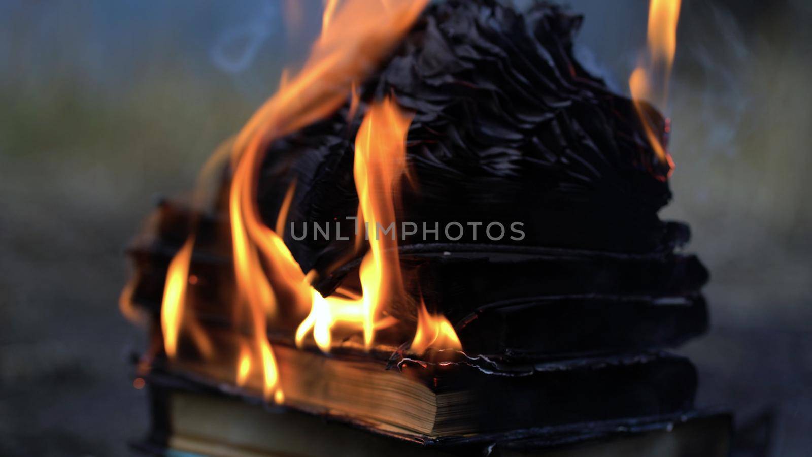 A stack of old books on fire burns on the ground.