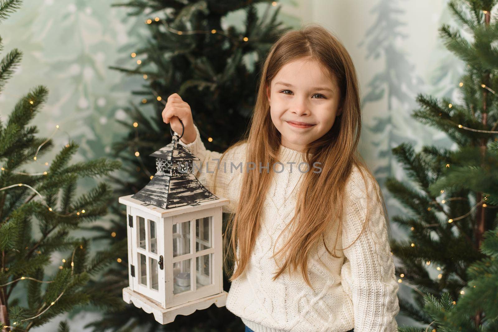 Cute baby girl holding a Christmas lantern among the Christmas trees