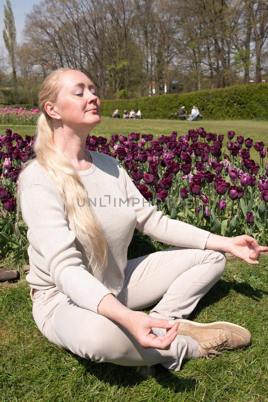 Young beautiful woman in the park with spring tulips does yoga on the lawn by KaterinaDalemans