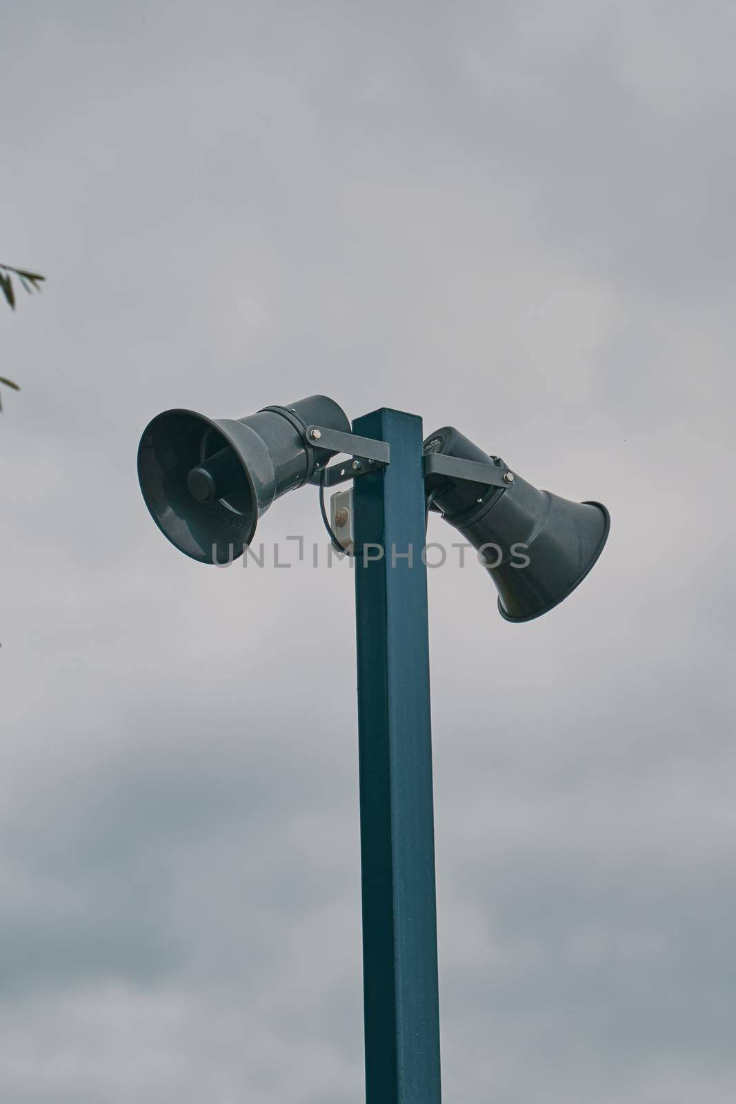 Tall metal column with two gray loudspeakers against cloudy sky. Hazard warning system. Providing security in the city, notification of emergencies.