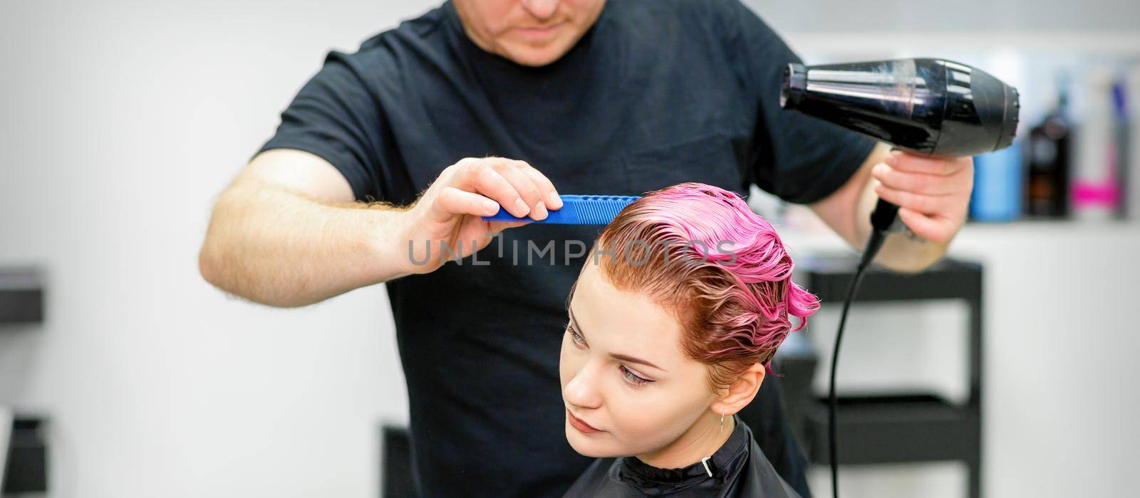 A hairdresser is drying the pink hair of the young woman in a beauty salon. by okskukuruza