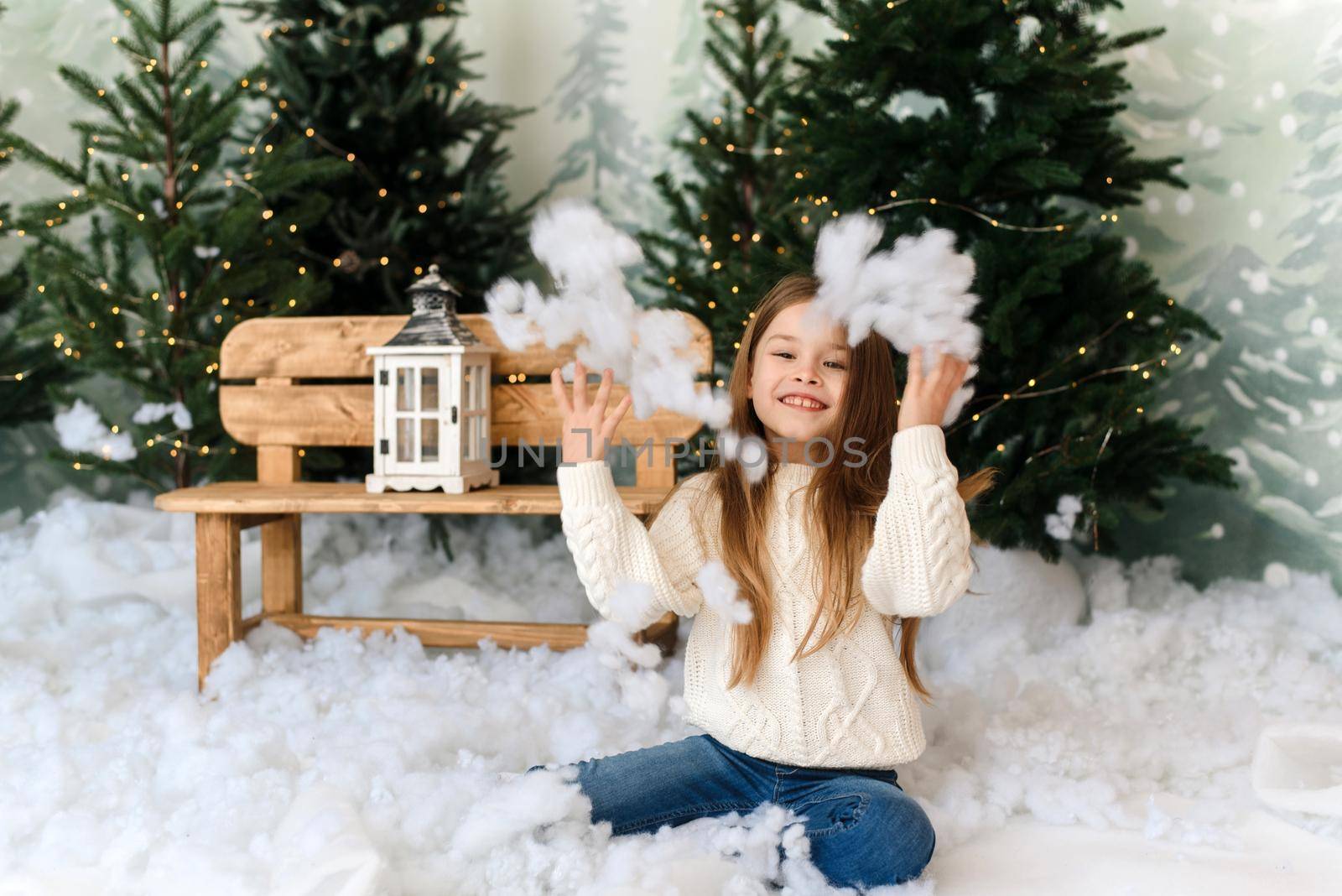 A little cute girl in the interior of the Christmas studio throws artificial snow and rejoices at Christmas eve. by etonastenka