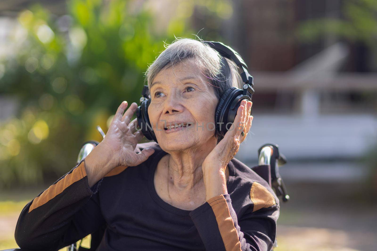 Asian senior woman listening music with headphone in backyard.