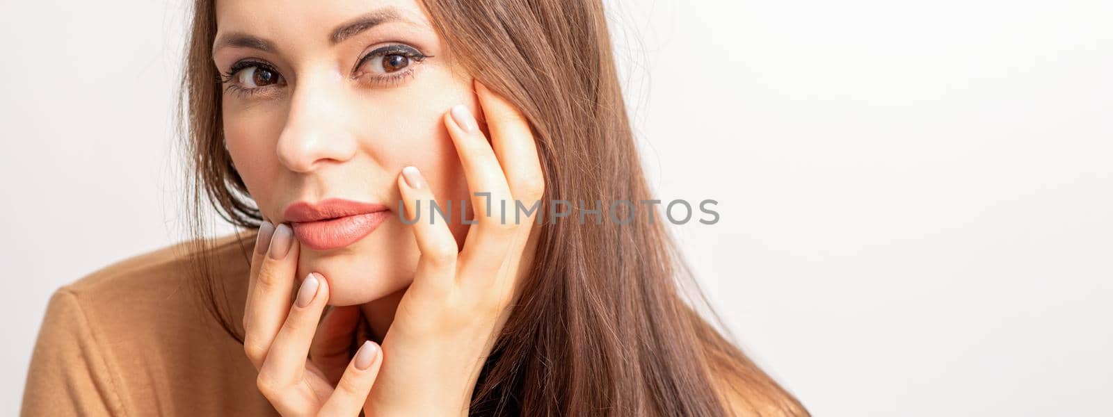 Portrait of the caucasian female model touching face with manicured fingers isolated on white background