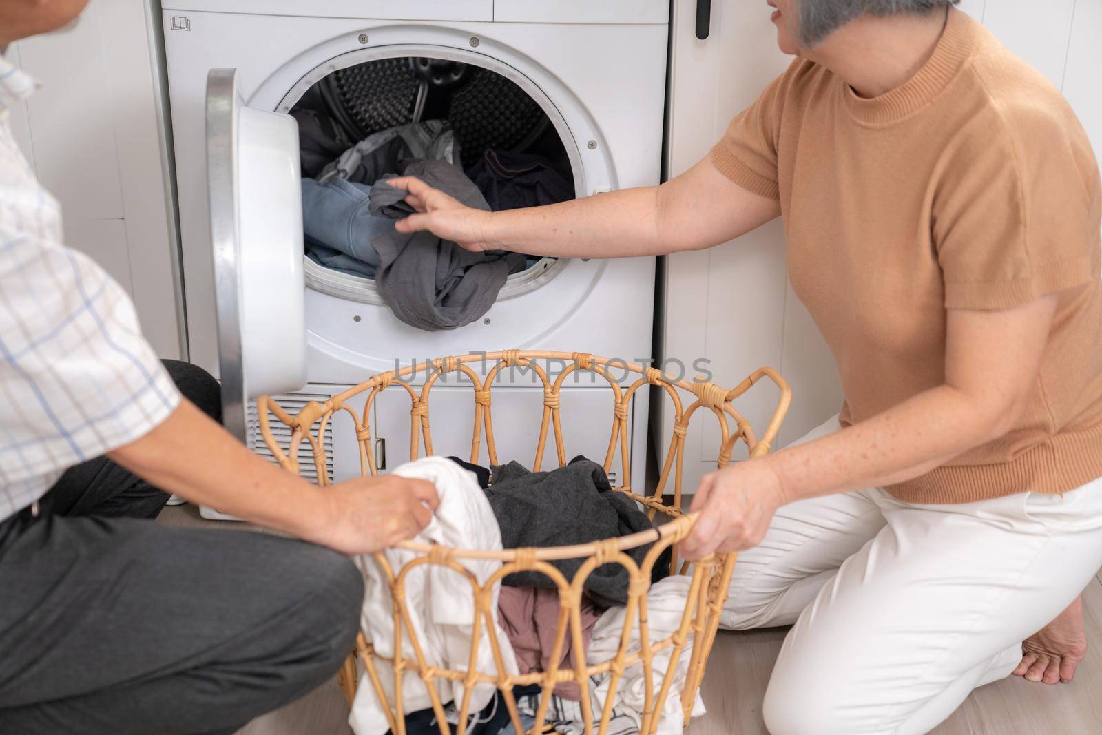 Senior couple working together to complete their household chores at the washing machine in a happy and contented manner. Husband and wife doing the usual tasks in the house.