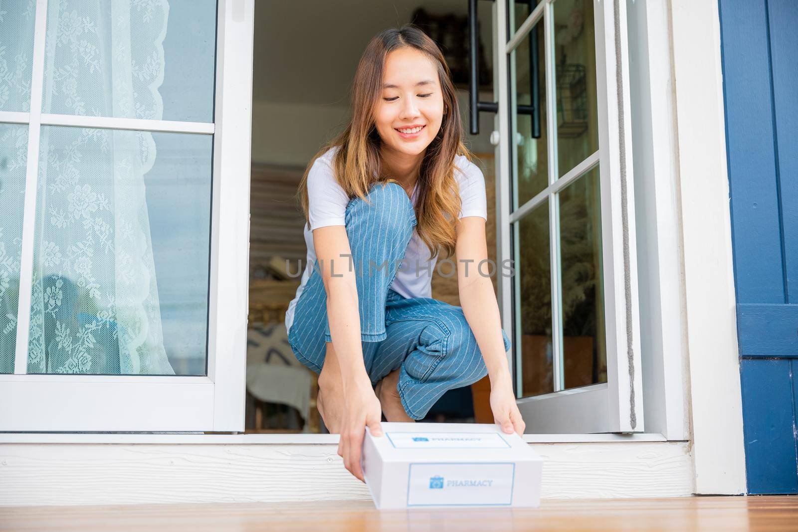 Close up hands of sick Asian woman sitting at door to receive medication first aid pharmacy box from hospital delivery service at floor home, female patient buy drugstore online business, healthcare