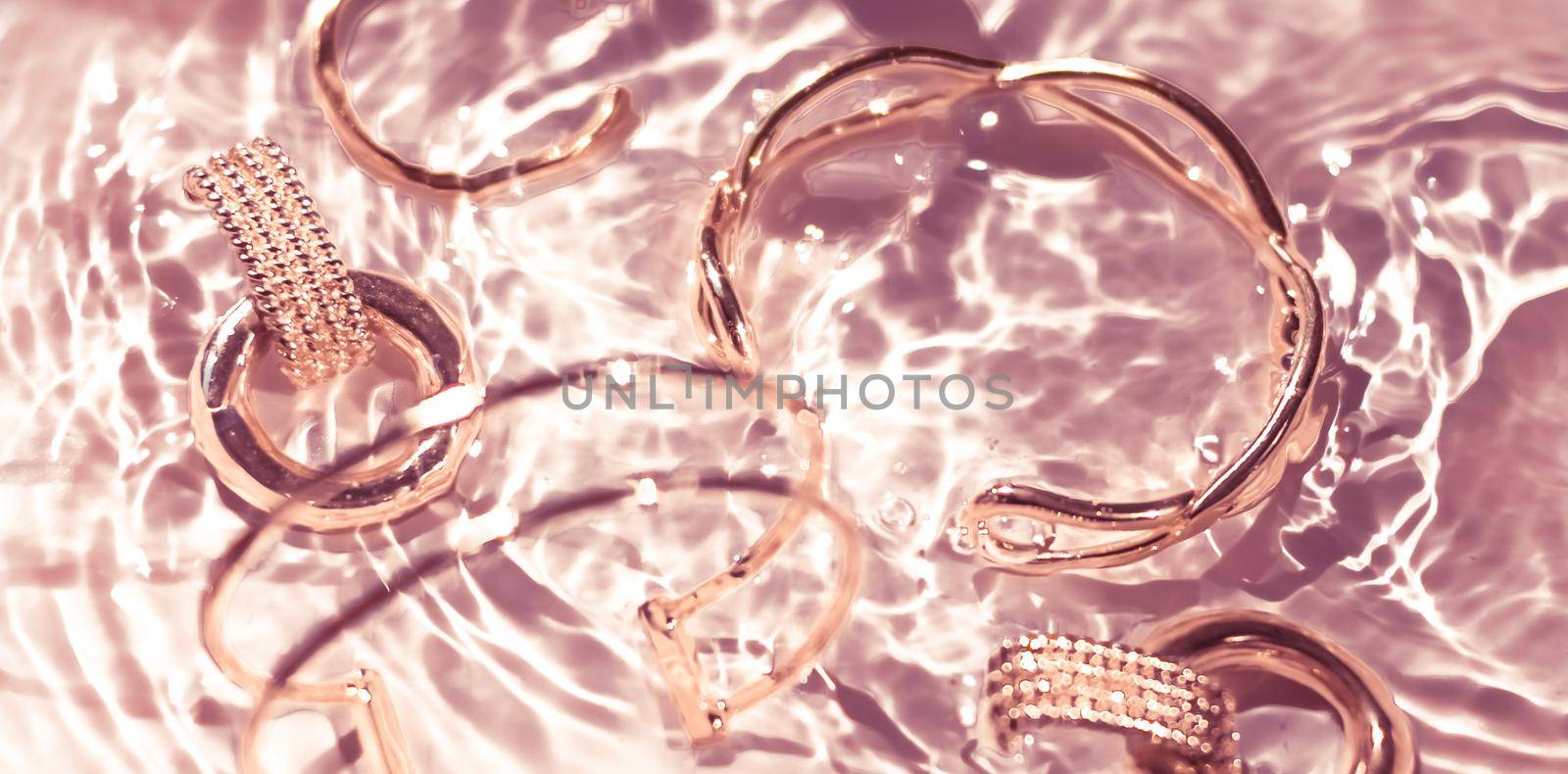 Rose gold bracelets, earrings, rings, jewelery on pink water background, luxury glamour and holiday beauty design for jewelry brand ads by Anneleven