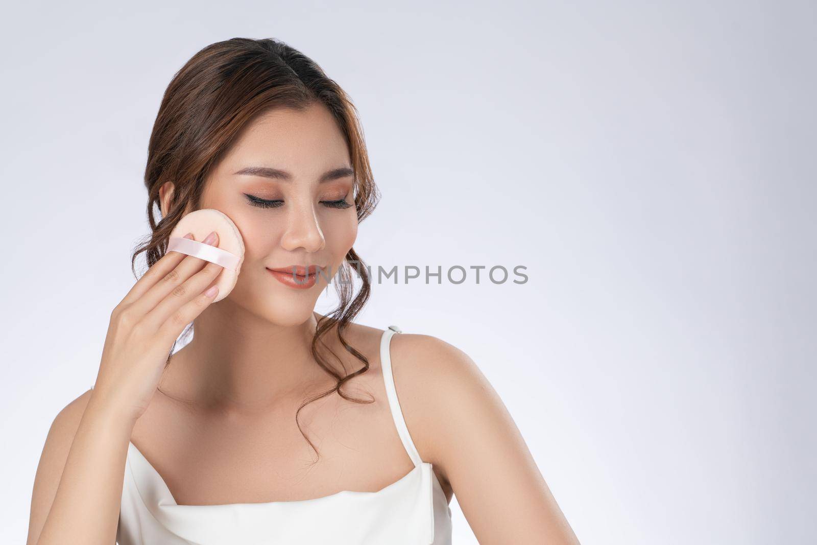 Face make up concept. Portrait of gorgeous young girl applying dry powder foundation. Beautiful model putting makeup powder with cosmetic cushion on her face.