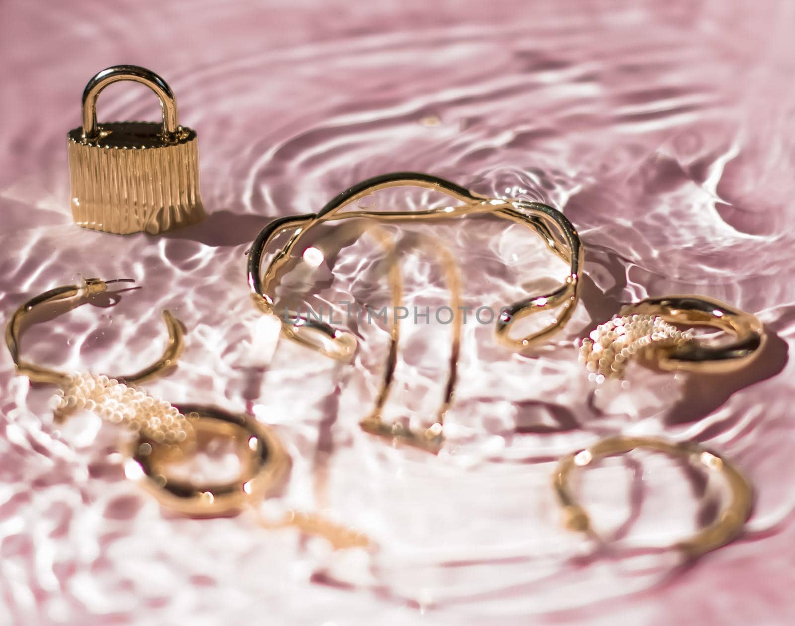 Golden bracelets, earrings, rings, jewelery on pink water background, luxury glamour and holiday beauty design for jewelry brand ads by Anneleven