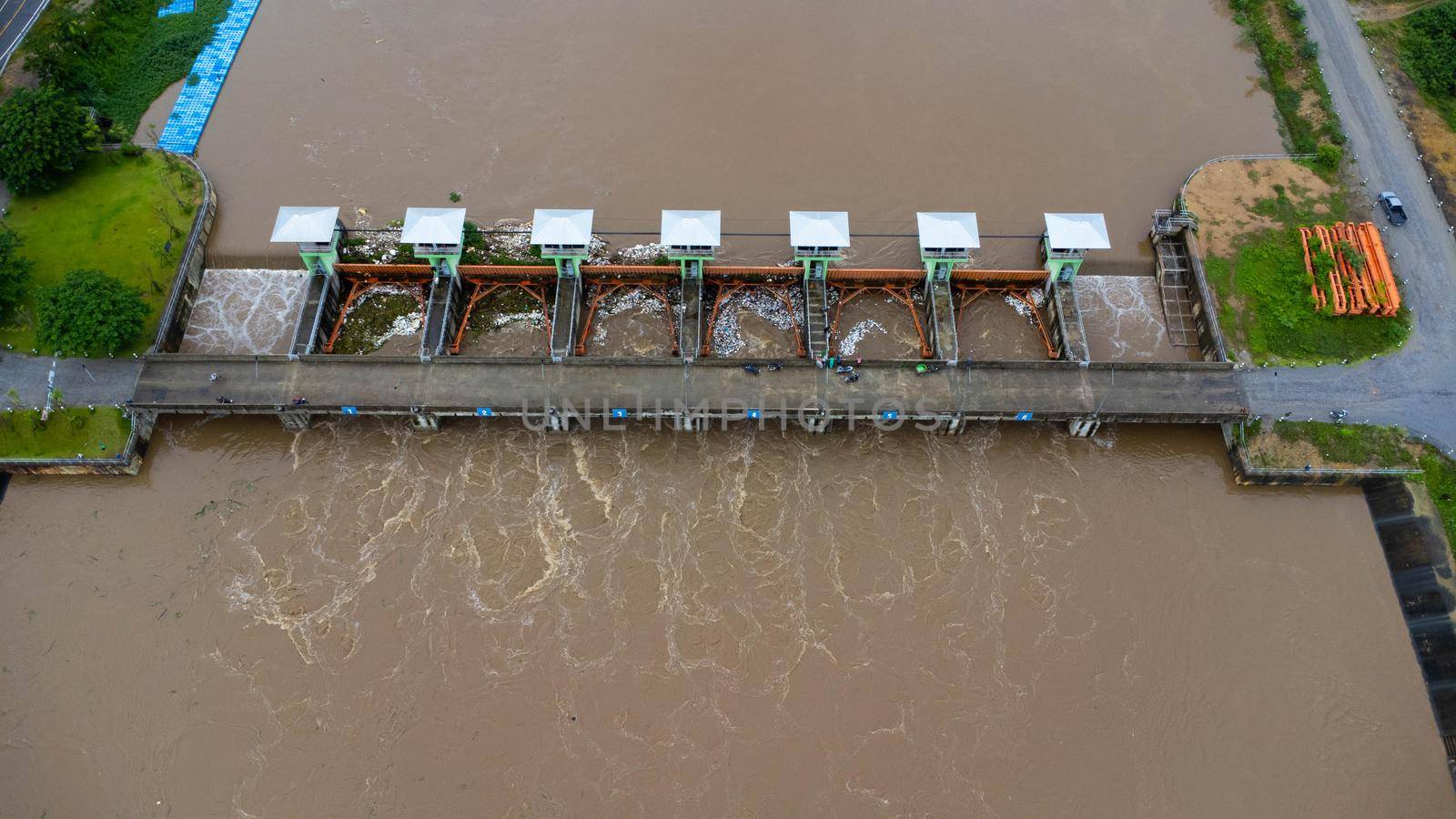 Aerial view of the water released from the concrete dam's drainage channel as the overflow in the rainy season. Top view of turbid brown forest water flows from a dam in rural northern Thailand. by TEERASAK