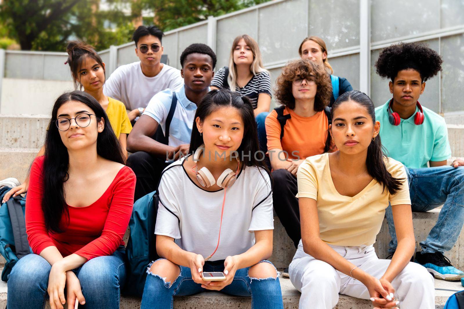 Group of multiracial teen high school students looking at camera sit on stairs outdoors. by Hoverstock