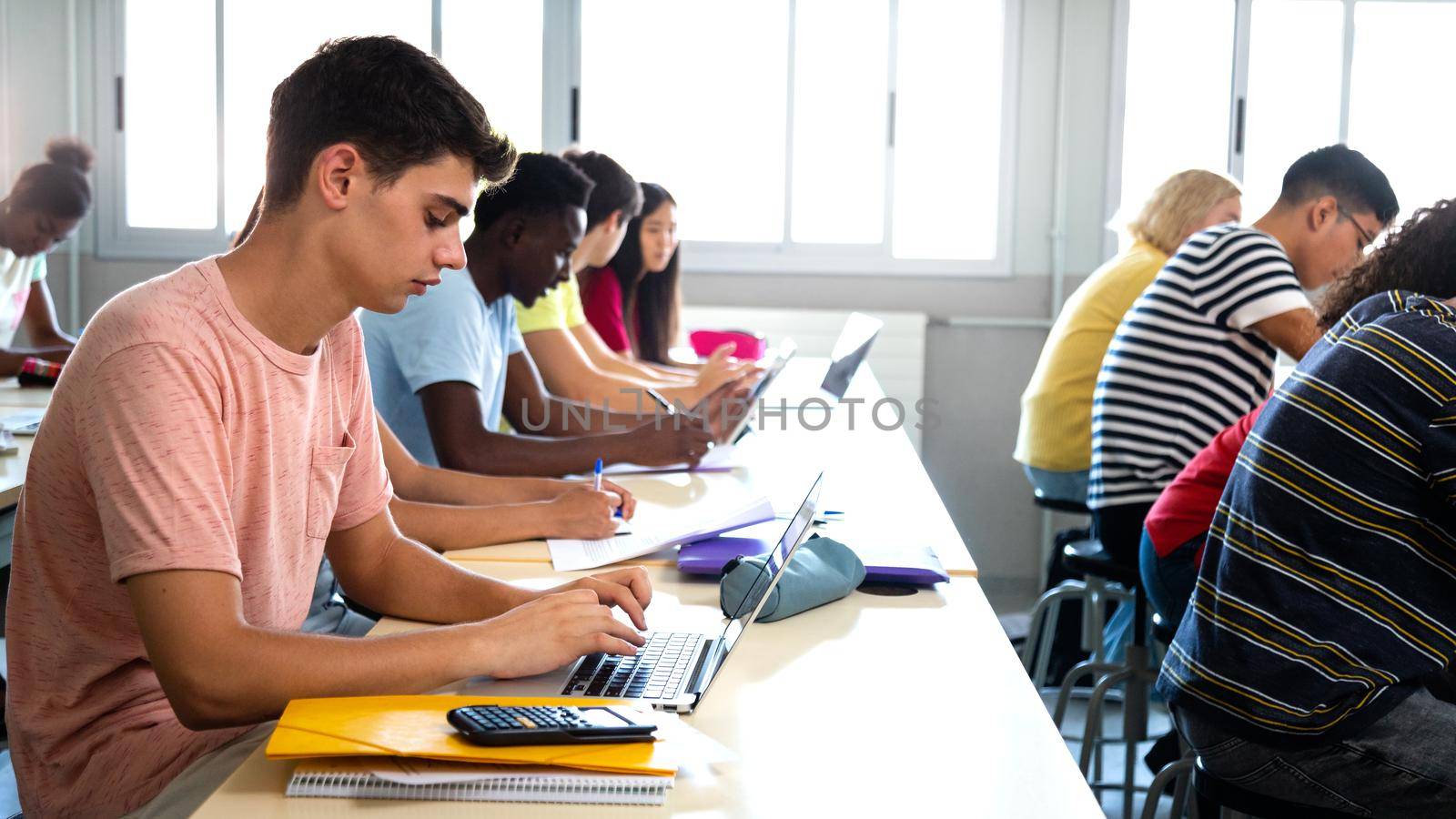 Side view of group of multiracial high school students studying and using laptops in class. by Hoverstock