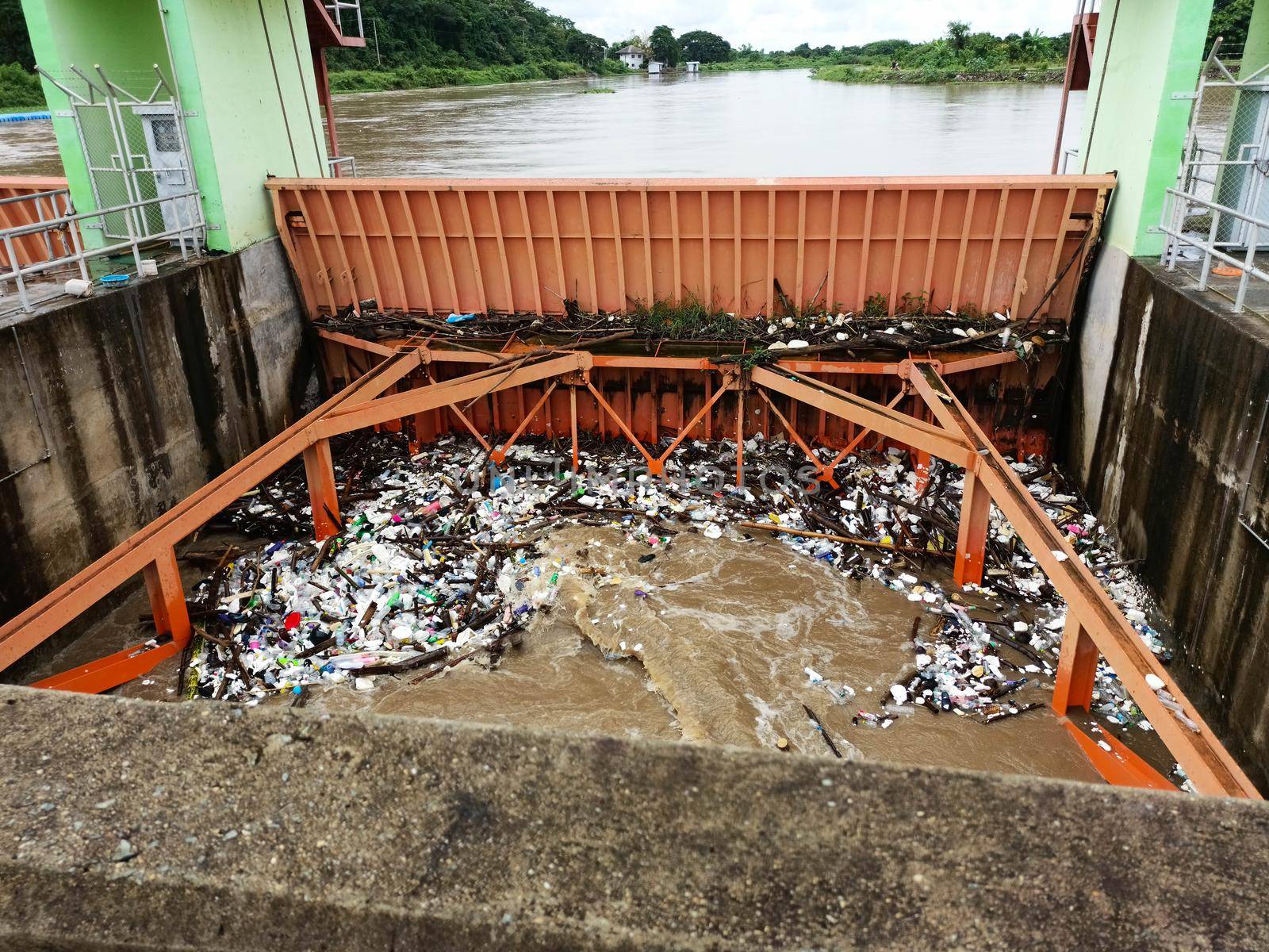 Aerial view of turbid brown forest water released by concrete dam drainage channels as water overflows in the rainy season with dry twigs and plastic waste at a dam gate in rural northern Thailand. by TEERASAK