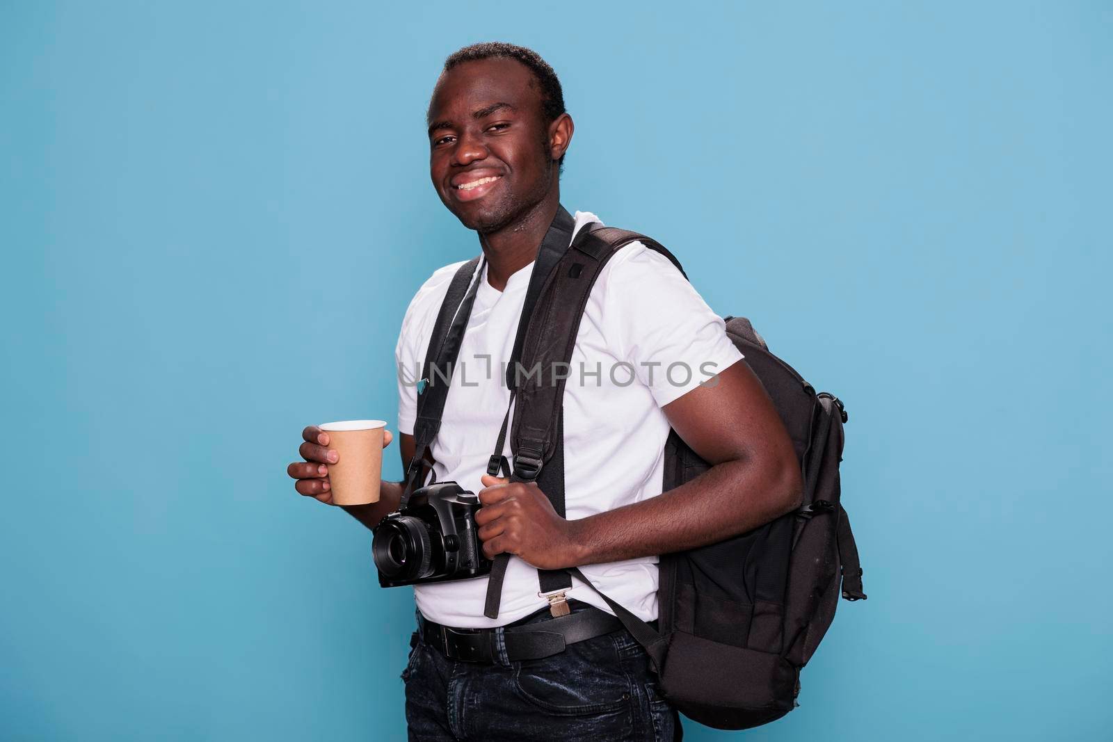 Smiling heartily photography enthusiast wearing travel backpack and professional camera ready for holiday trip. Confident tourist having DSLR device while being excited for citybreak.