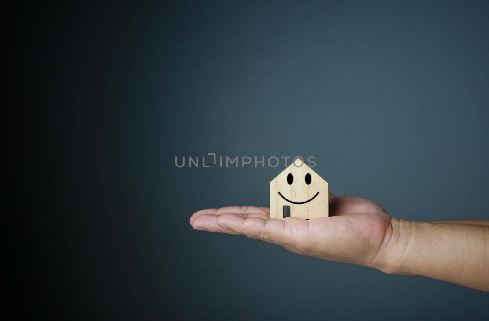 Happy house concept. Hand holding a smiling model house. Indicates happiness and love in the house. by Unimages2527