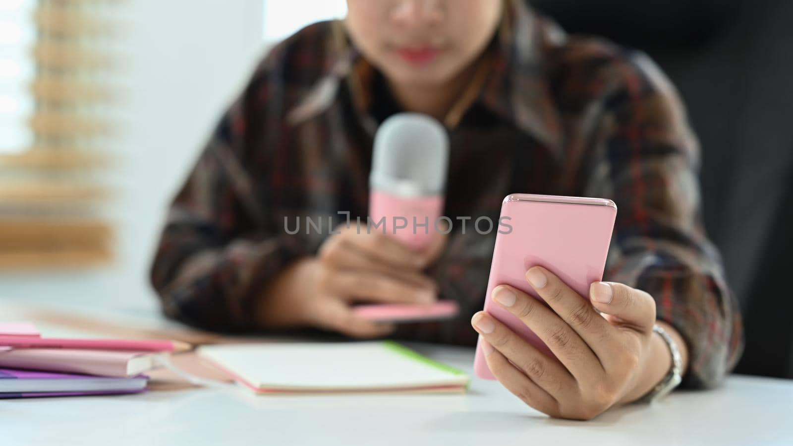 Cropped image of young woman using smart phone during recording podcast in broadcasting home studio.