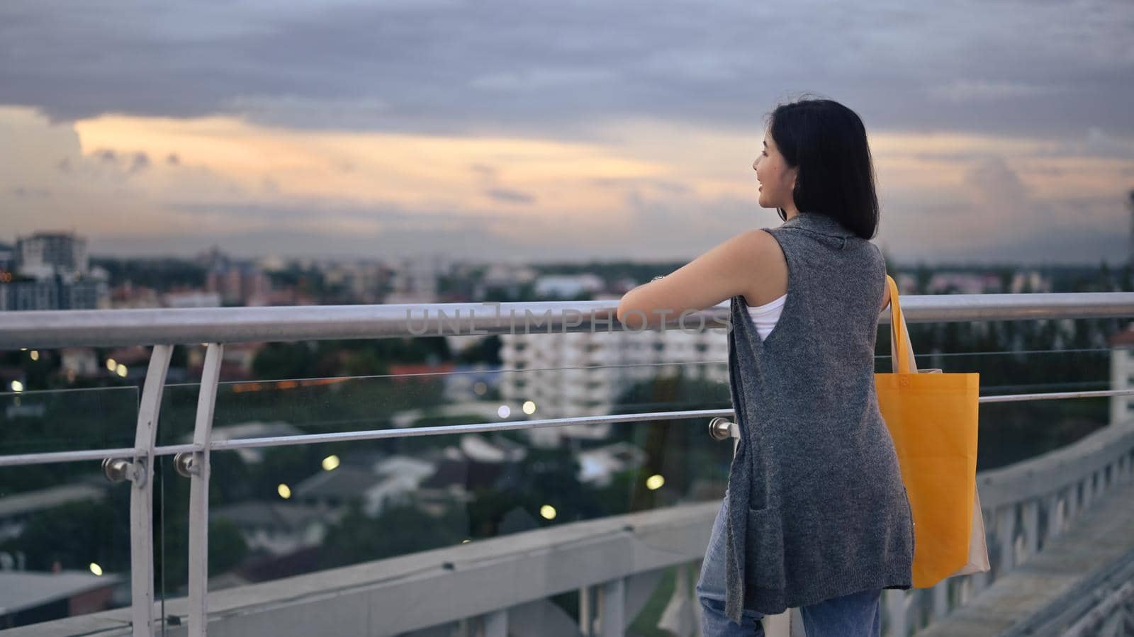 Rear view of asian woman standing on rooftop terrace with overlooking the city at sunset view by prathanchorruangsak