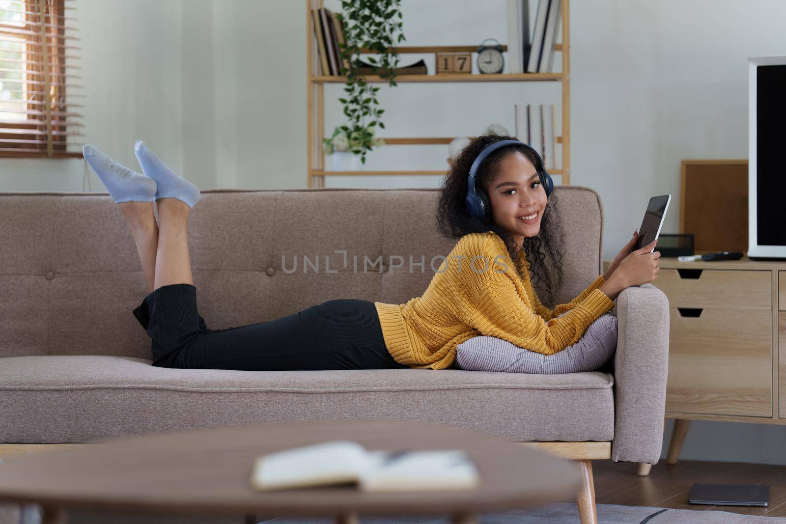 Attractive smiling young woman using tablet and listen music on sofa at home. lifestyle concept by itchaznong