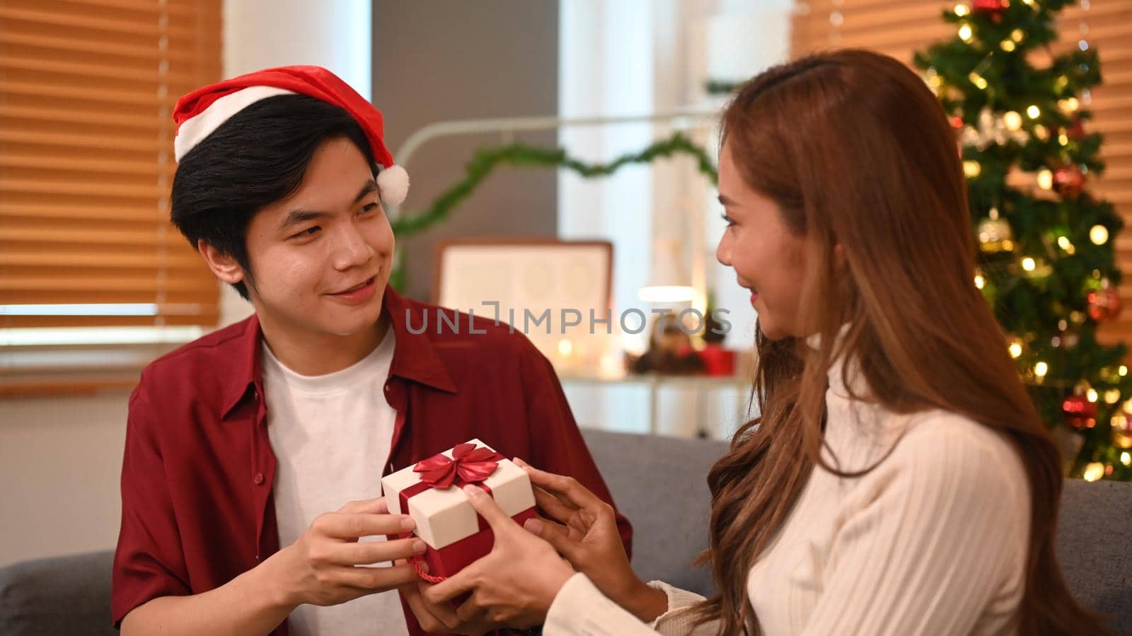 Young man giving surprise gift to his girlfriend during celebrating New Year at home. Family, holidays and people concept by prathanchorruangsak