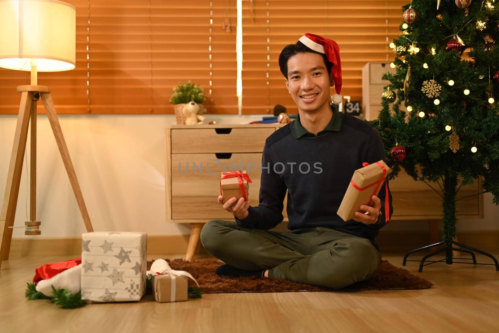 Cheerful man sitting on floor in living room and preparing Christmas gifts. Celebration, holidays and Christmas concept.