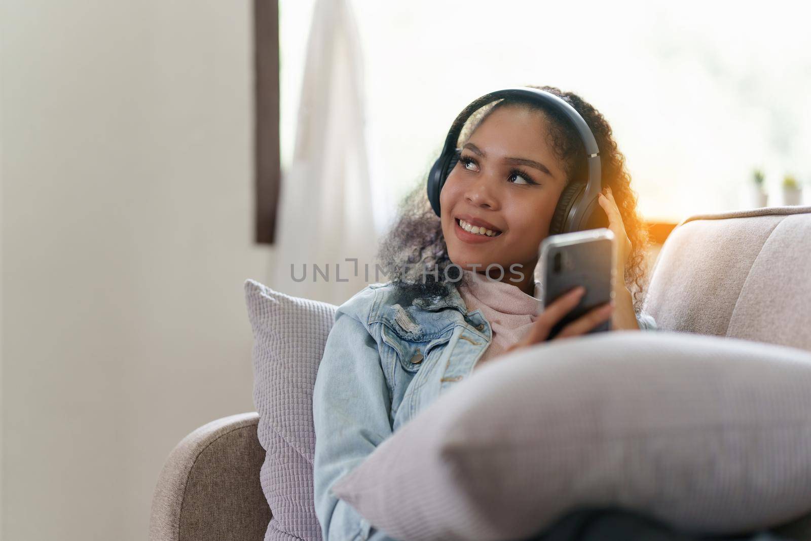 Attractive smiling young woman using mobile phone and listen music on sofa at home. lifestyle concept.
