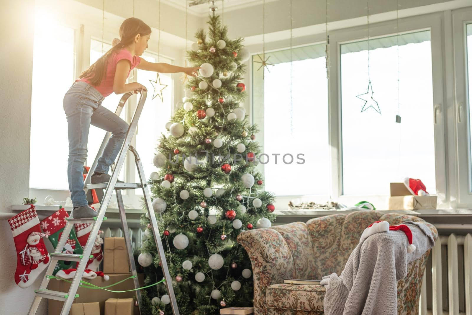 little girl on a stepladder decorating Christmas tree.