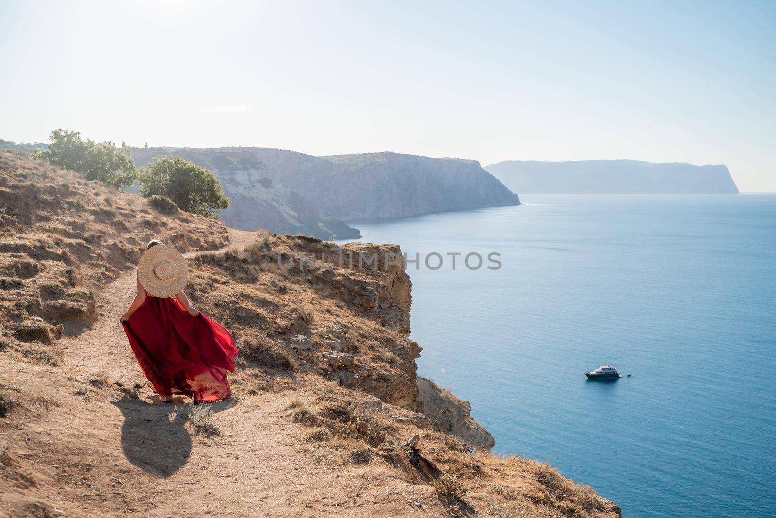 A woman in a red flying dress fluttering in the wind, against the backdrop of the sea