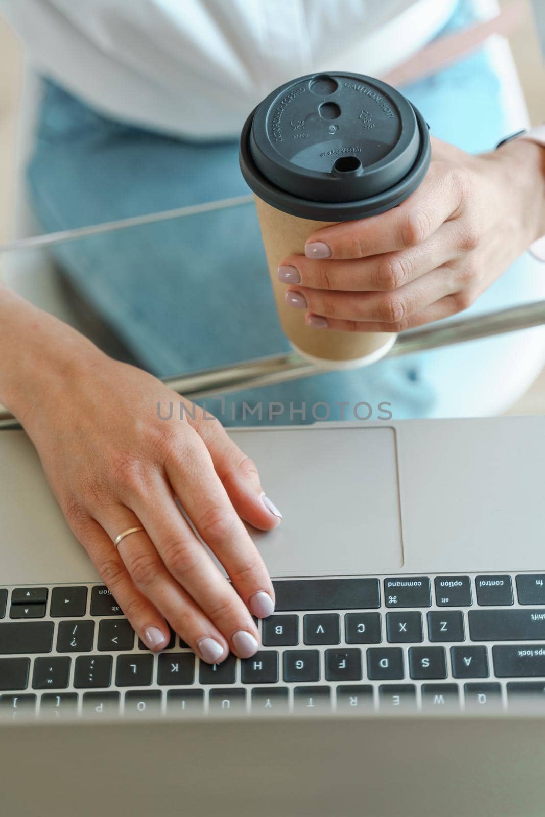 Hands typing on a computer keyboard over a white office table with a cup of coffee and supplies, top view. by Matiunina