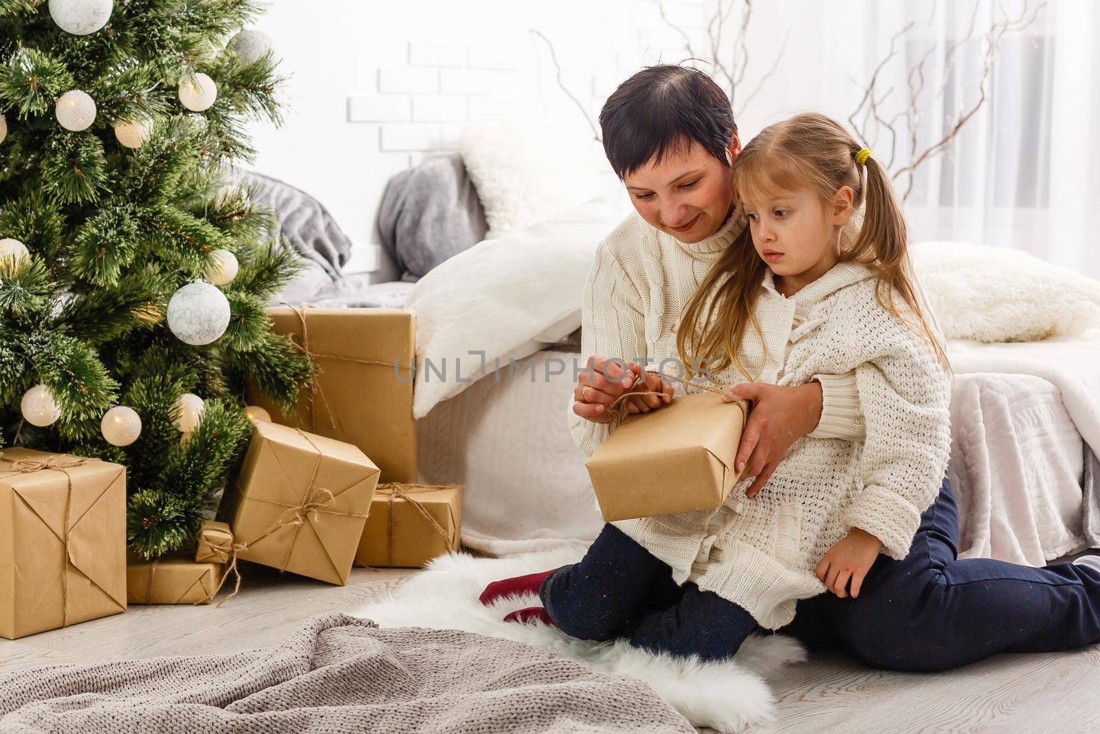 holidays, celebration, family and people concept - happy mother and little girl with gift box over living room and christmas tree background by Andelov13