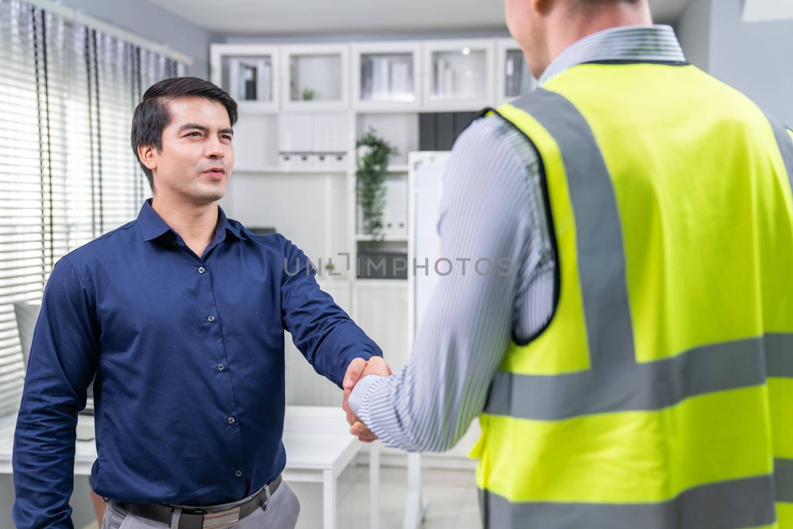 An engineer with a protective vest handshake with an investor in his office by biancoblue