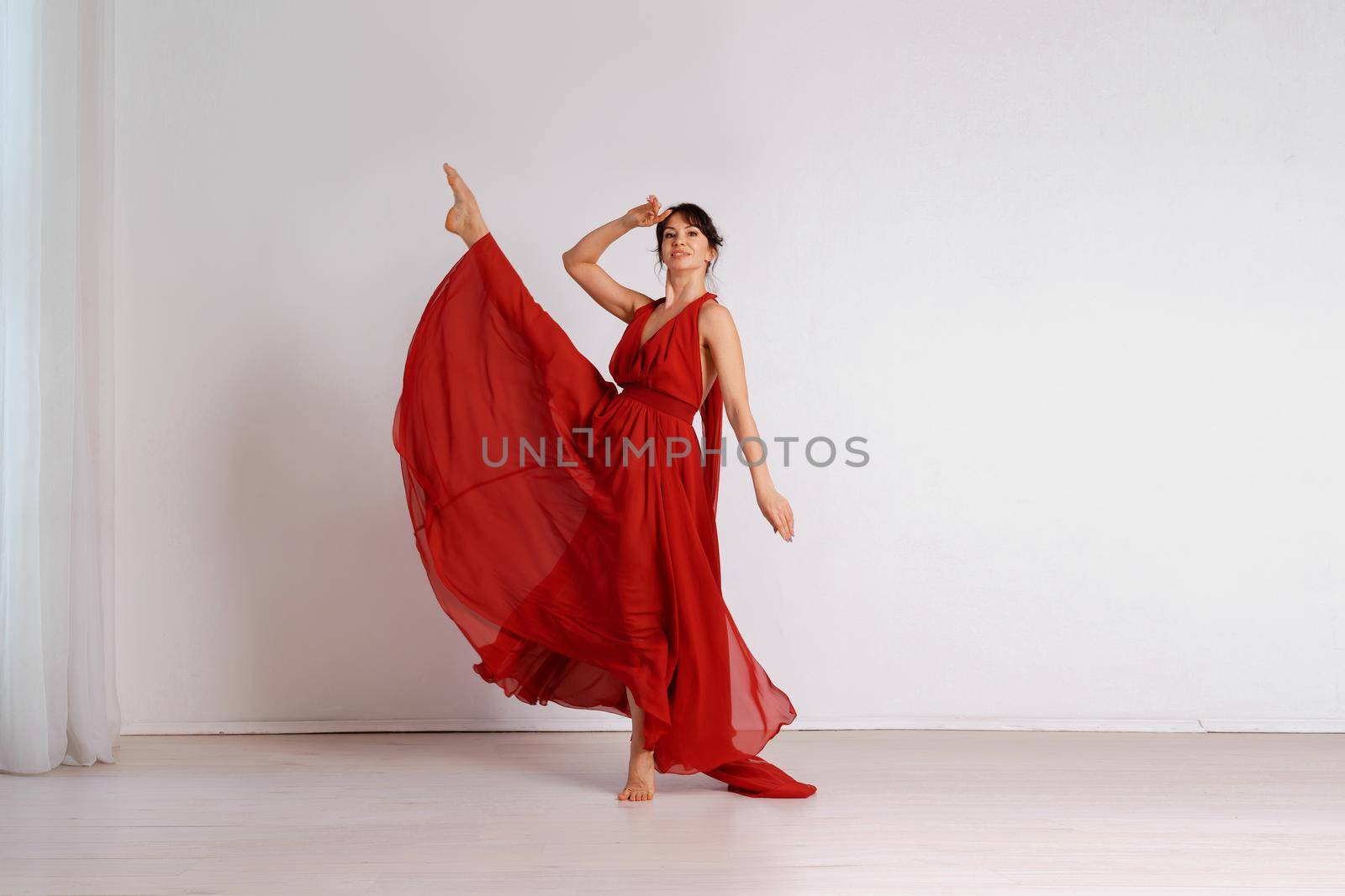 Dancer in a red flying dress. Woman ballerina dancing on a white studio background.