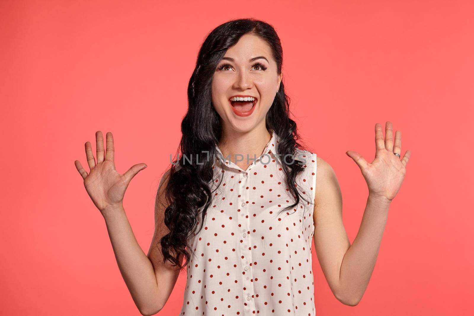 Studio shot of a gorgeous adolescent girl, wearing casual white polka dot blouse. Little brunette female is smiling widely and looking very happy posing over a pink background. People and sincere emotions.