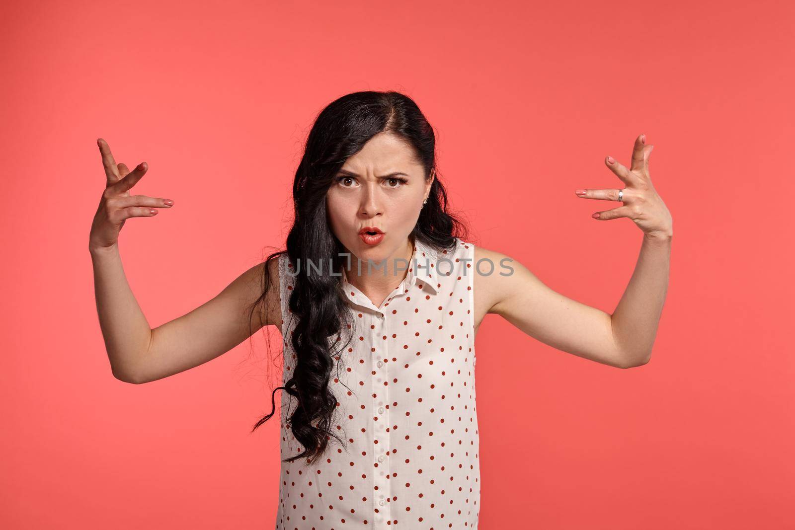 Studio shot of a good-looking teen lady, wearing casual white polka dot blouse. Little brunette female gesticulating while posing over a pink background. People and sincere emotions.