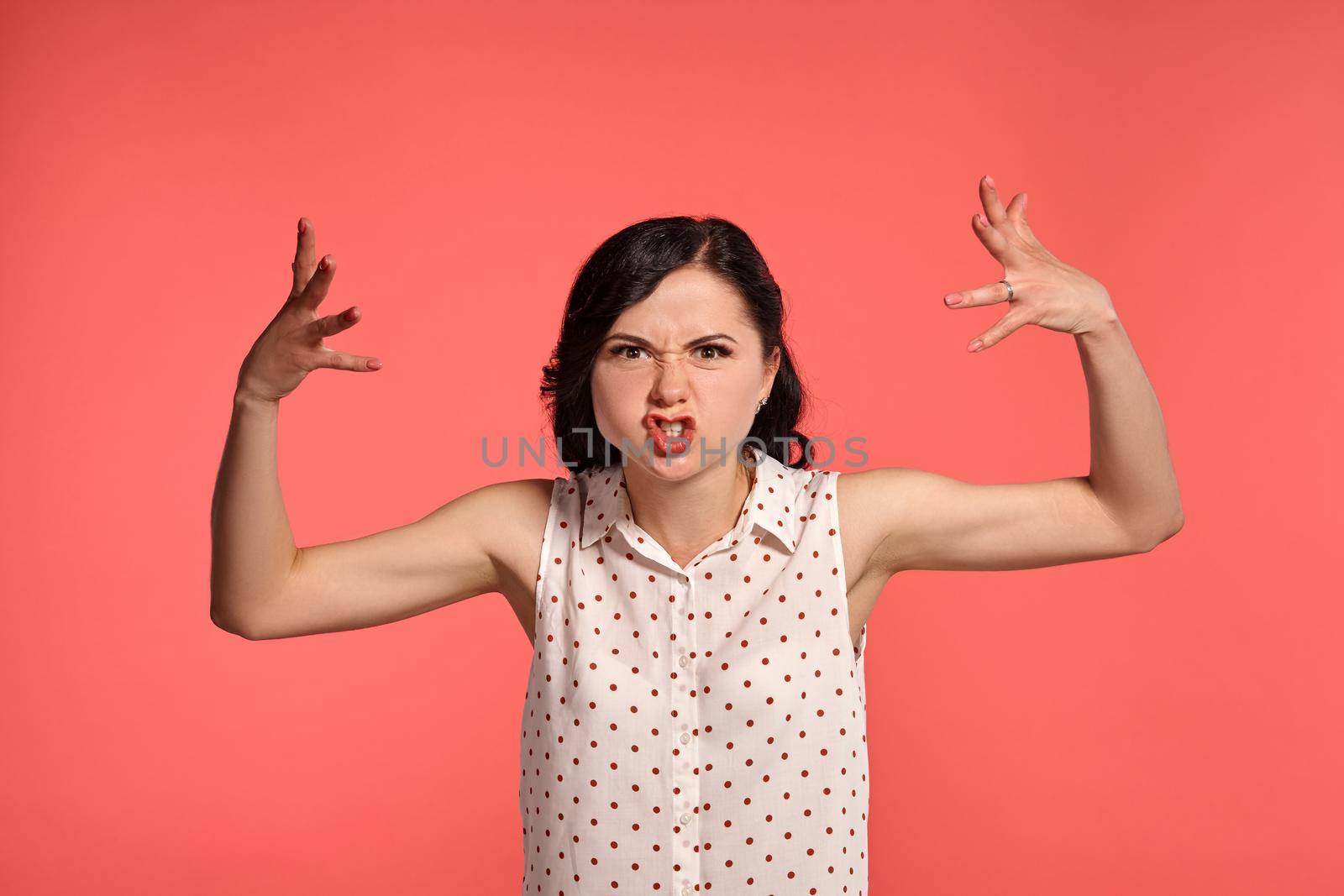 Studio shot of an adorable teen lady , wearing casual white polka dot blouse. Little brunette female looking mad, posing over a pink background. People and sincere emotions.