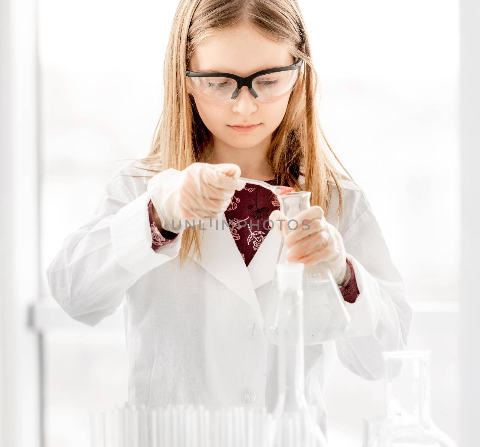 Smart girl doing scientific chemistry experiment wearing protection glasses. Preteen schoolgirl with equipment and chemical liquids on school lesson
