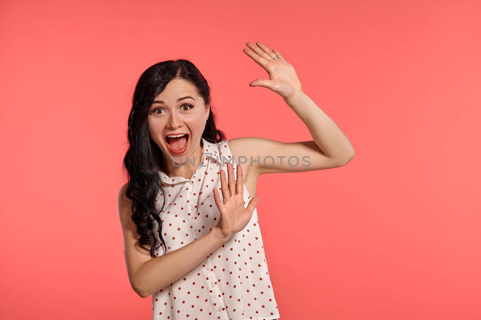 Studio shot of an alluring teeny girl, wearing casual white polka dot blouse. Little brunette female feeling happy, posing over a pink background. People and sincere emotions.