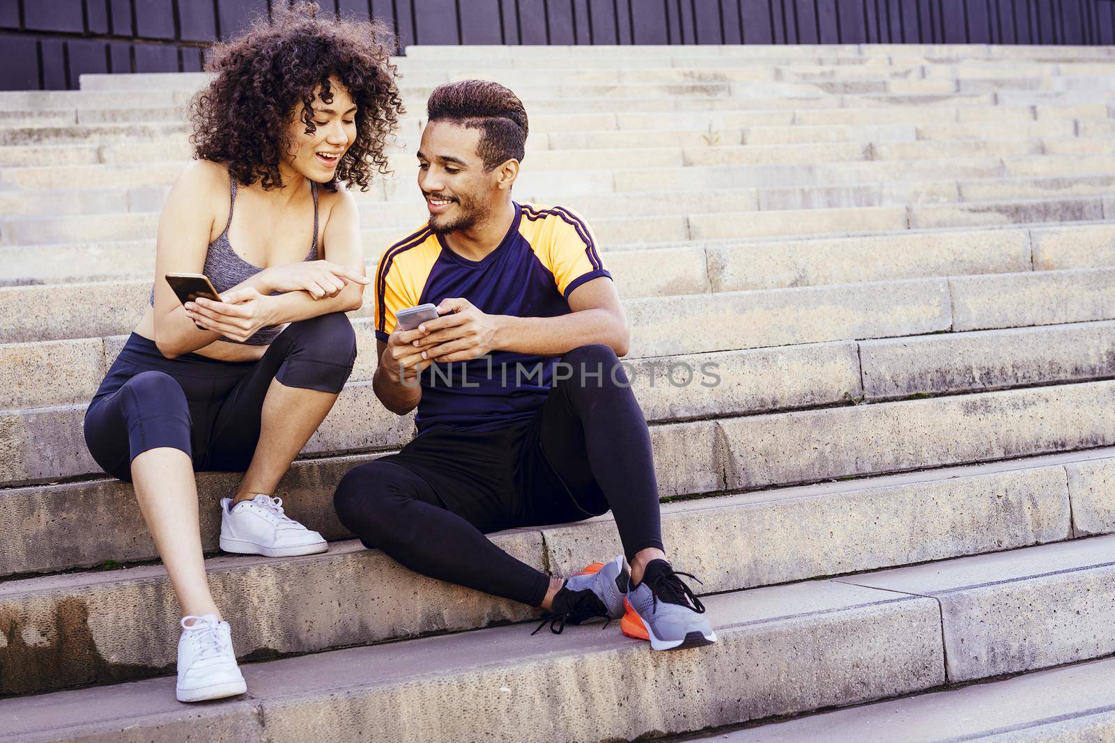 happy athletic young couple looking the sports app in their mobile phone on the stairs during a rest in the workout, technology in sport and healthy lifestyle concept