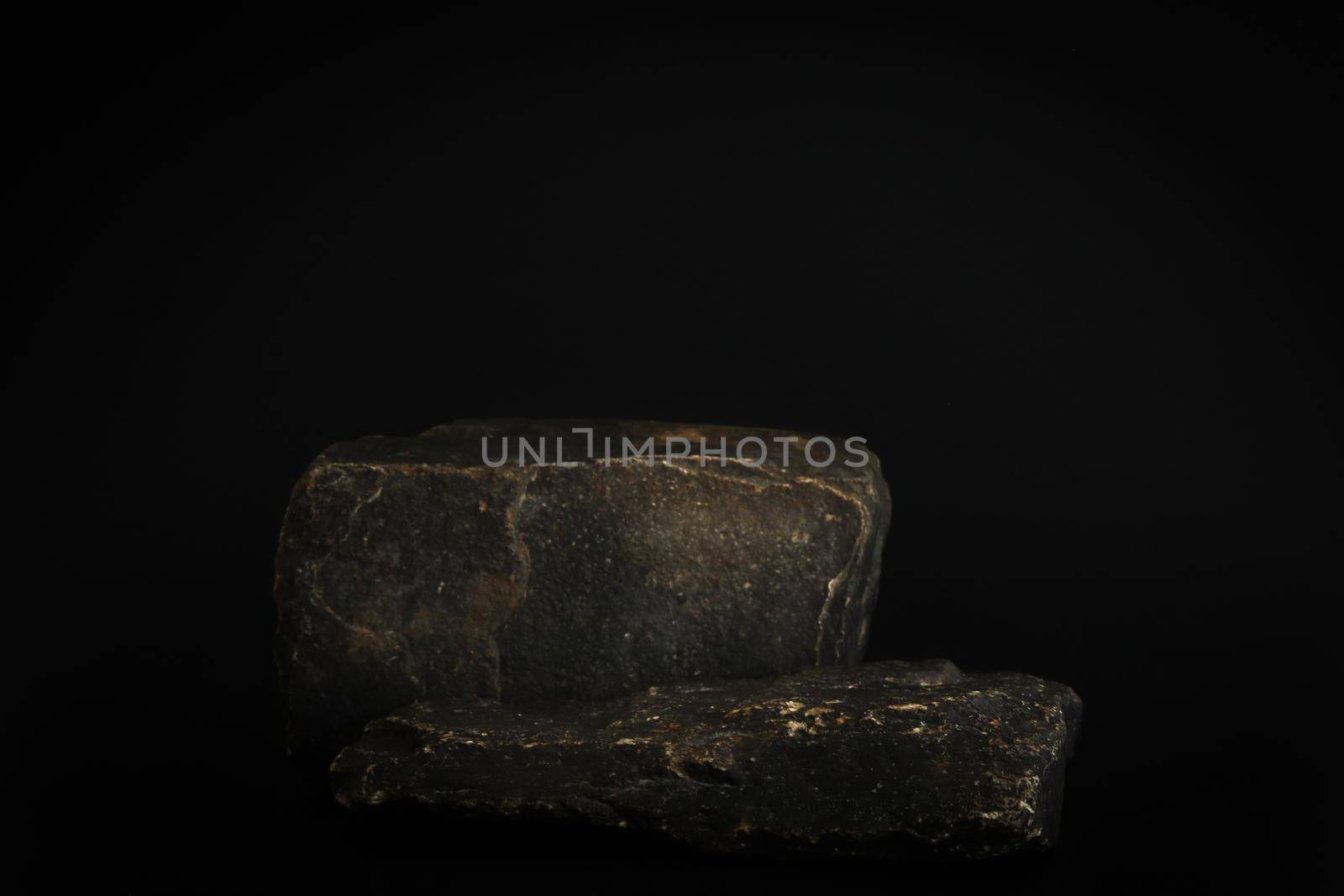 Rock podium on the black background. Stone podest for product, cosmetic presentation. Creative mock up. Pedestal or platform for beauty products