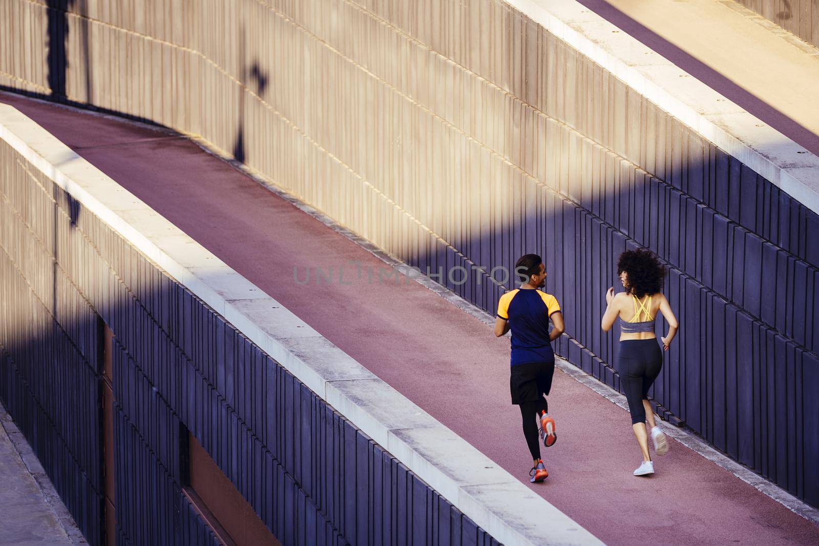 rear view of an interracial couple of runners jogging on the city street in modern environment of walls. fitness, urban sports workout and healthy lifestyle concept, copy space for text