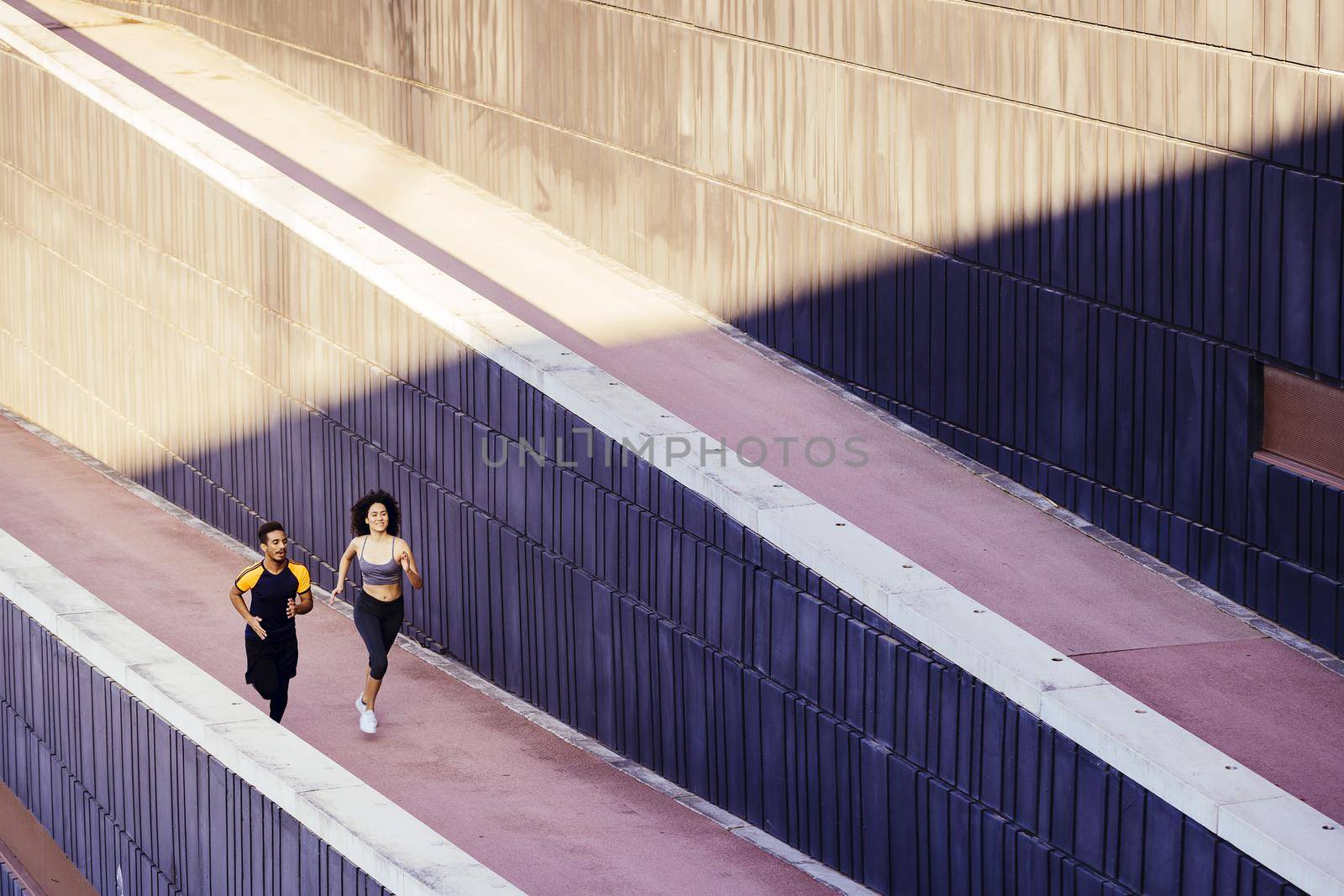 happy young woman and sports man running on the city street in modern environment of walls. fitness, urban sports workout and healthy lifestyle concept, copy space for text