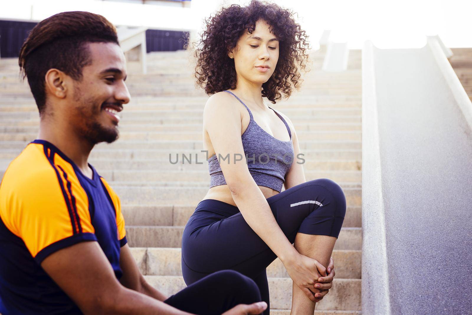 young latin woman and afro american man stretching on city stairs before running. fitness, urban sports workout and healthy lifestyle concept, copy space for text
